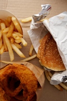 Photo of generic fast food, including French fries, a hamburger and onion rings.