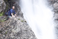 Photo of a man on his knees next to a waterfall, looking with wonder, illustrating praising God.