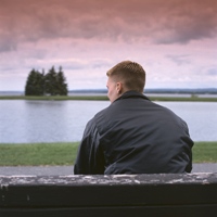 Photo of a man sitting on a bench thinking as sunset approaches.