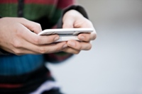 Close-up photo of a teen texting on a cell phone.