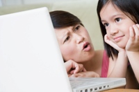 Photo of a Tiger Mother looking disapprovingly at daughter who is looking at a laptop screen